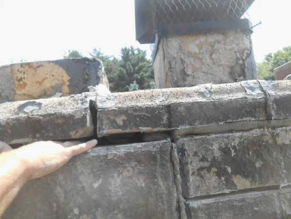 Large Gaps In Mortar of chimney tech's hand stuck in between gaps with trees in the background.