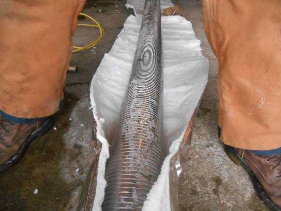 Metal Chimney Liner Wrapped With Insulation in between a man's feet and shoes