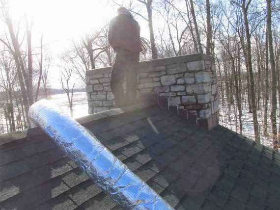 man working on chimney standing on roof near chimney with metal liner across the roof