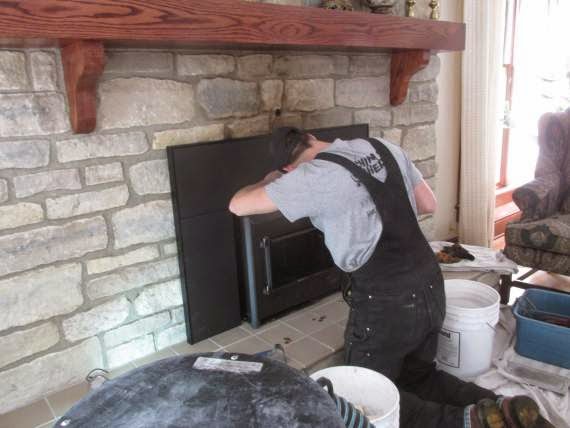 man in black overalls and hat working to install chimney liner in fireplace buckets surround him