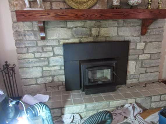 New fireplace insert shown on chimney hearth of a home area around the front stones have been cleaned up. Nice wooden mantel.  Tools and equipment in foreground.