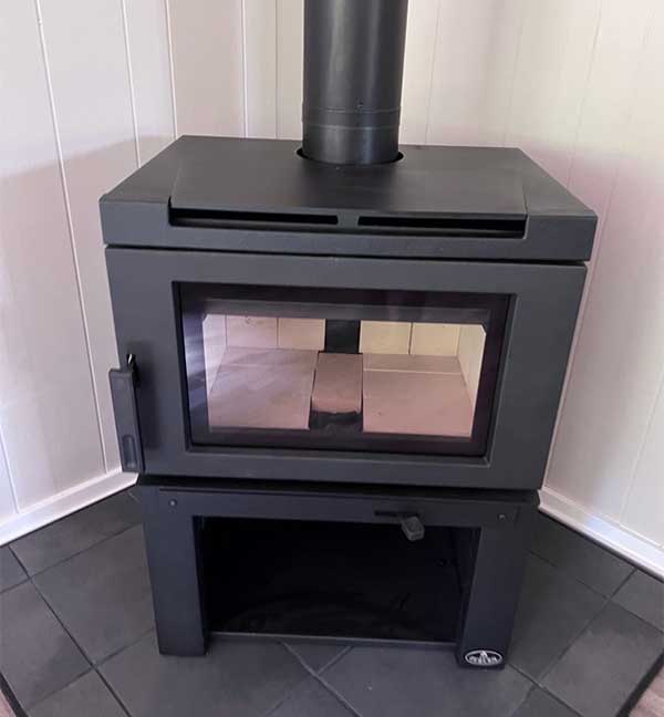 Osburn Matrix free-standing black stove standing in corner with tile underneath and pipe going through the ceiling.